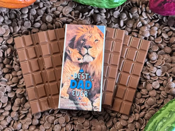 'Best Dad Ever' chocolate bar in packaging, placed over chocolate bars without packaging and on top of a bed of chocolate drops.