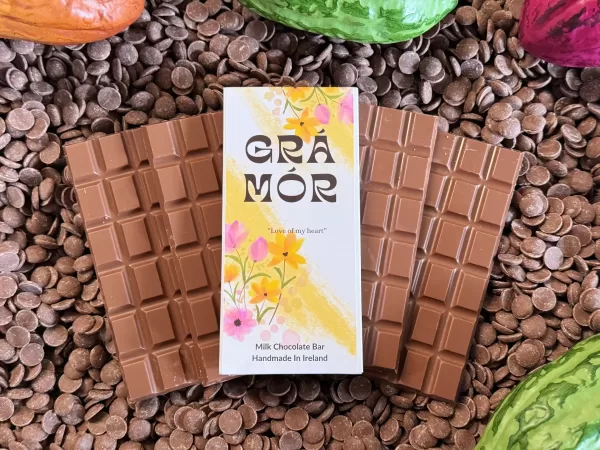 Grá Mór chocolate bar in packaging, placed over chocolate bars without packaging and on top of a bed of chocolate drops.