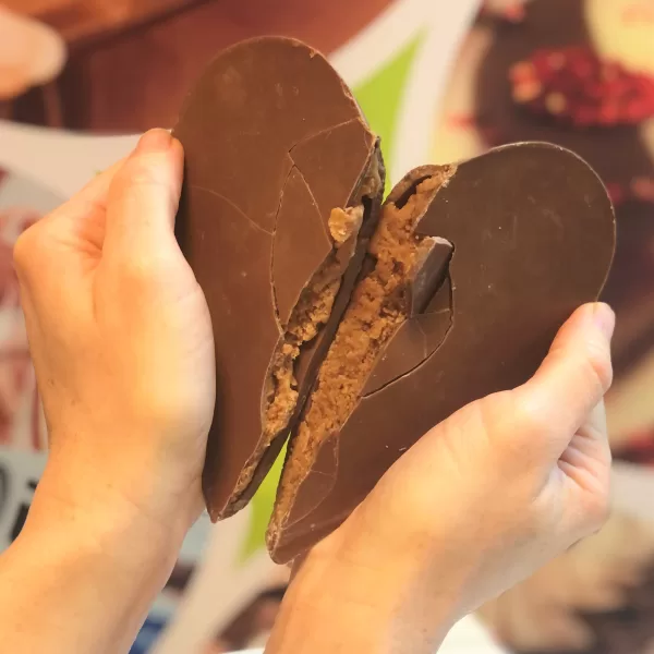 Hands are displayed breaking open a milk chocolate praline heart.