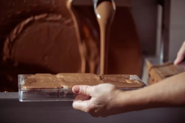 A mould has been filled with chocolate while chocolate flows in the background.