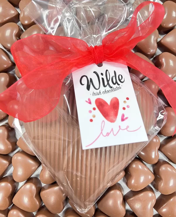 Milk Chocolate praline sharing heart tied with a red bow and displayed on a bed of heart shaped chocolates.