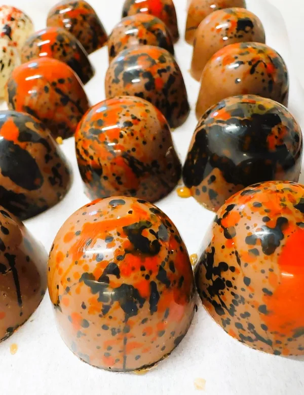 Rows of dome-shaped chocolates with shiny brown coating and bold orange and black splatter design.